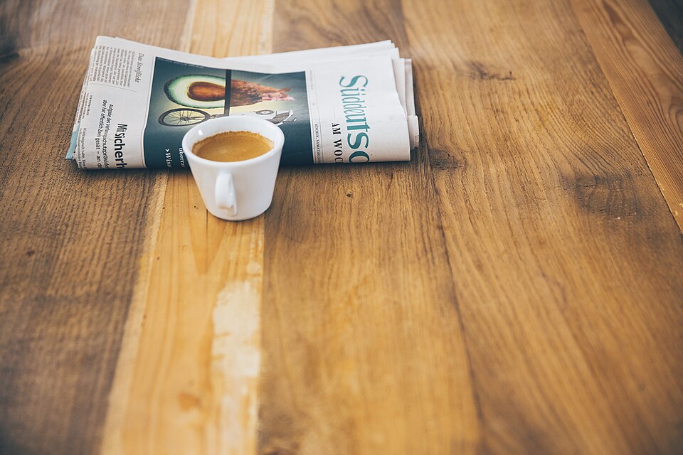 木のテーブルに置かれたコーヒーカップと新聞