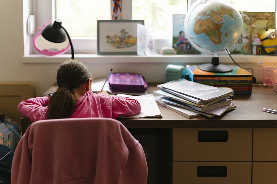 窓辺の机で書きものをする子どもの後ろ姿