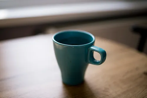 A bright turquoise mug is placed on a wooden table near a window, filled with steaming beverage. The morning light enhances the serene atmos